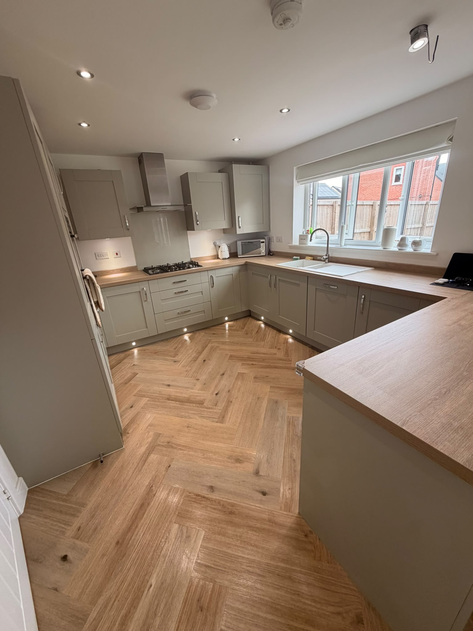 A clean kitchen with pale cabinets, wood worktops and herringbone flooring